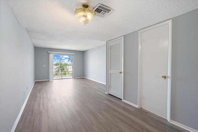 unfurnished room featuring wood finished floors, baseboards, a textured ceiling, and visible vents
