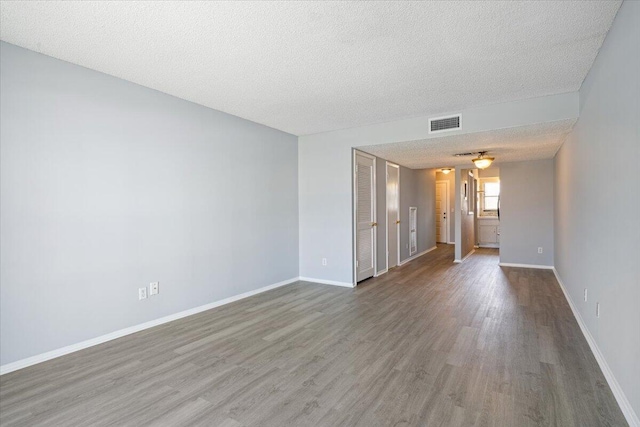 spare room with a textured ceiling, baseboards, wood finished floors, and visible vents