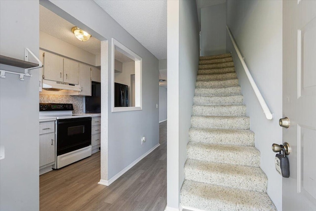stairway featuring baseboards, a textured ceiling, and wood finished floors