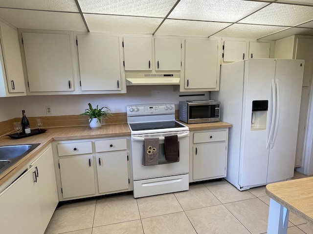 kitchen with white appliances, under cabinet range hood, light tile patterned floors, light countertops, and a drop ceiling
