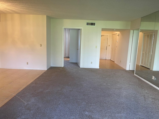 carpeted spare room with tile patterned floors, a textured ceiling, and baseboards