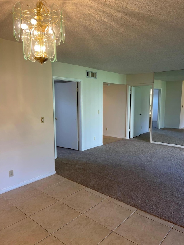 carpeted empty room featuring a chandelier, a textured ceiling, tile patterned flooring, and baseboards