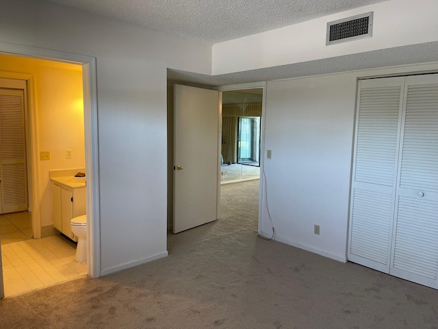 unfurnished bedroom featuring carpet flooring, a textured ceiling, ensuite bathroom, a closet, and baseboards