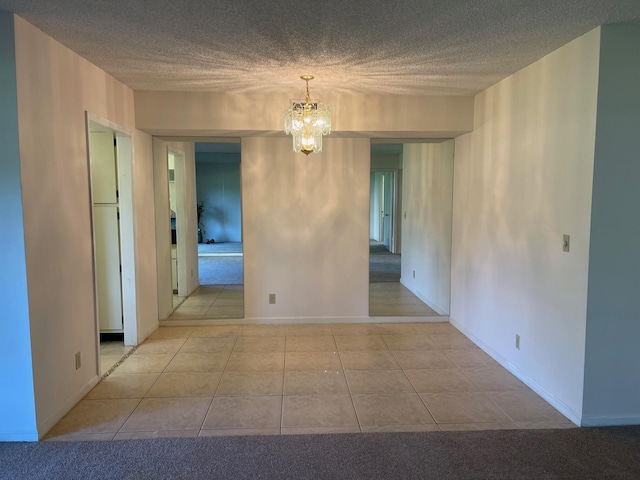spare room with a chandelier, tile patterned floors, a textured ceiling, and baseboards