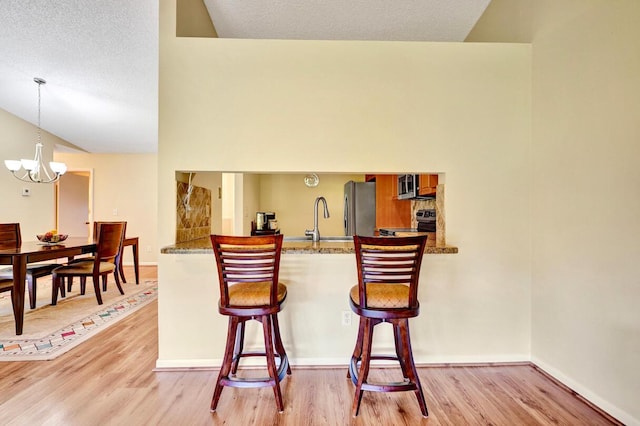 124 Mayfair Ln, Boynton Beach, FL 33426 - bar area with stainless steel appliances, light wood finished floors, a chandelier, vaulted ceiling, and decorative light fixtures
