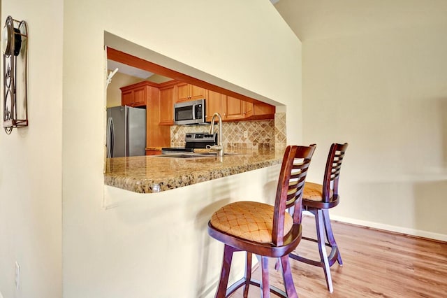 124 Mayfair Ln, Boynton Beach, FL 33426 - kitchen featuring appliances with stainless steel finishes, decorative backsplash, light wood finished floors, a kitchen bar, and light stone countertops