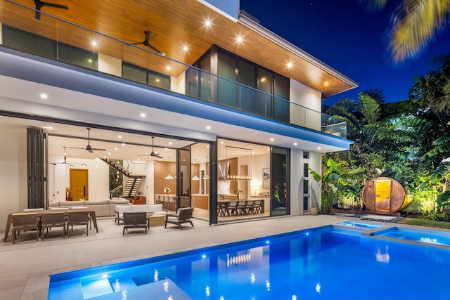 back of house at twilight featuring ceiling fan, a patio, a pool with connected hot tub, outdoor lounge area, and a balcony