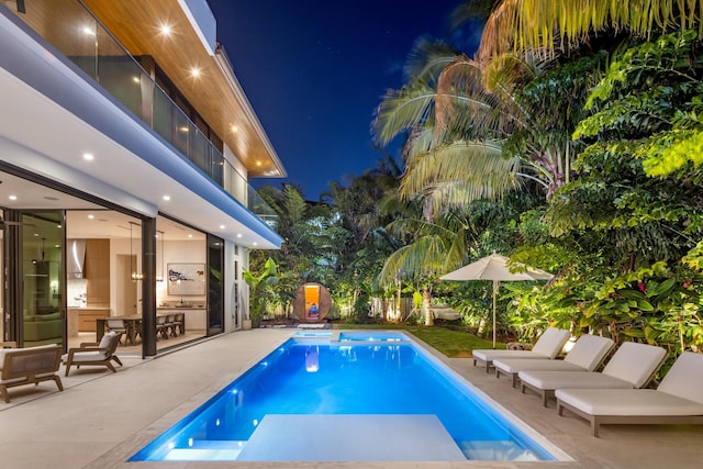 pool at night with a patio and a fenced in pool