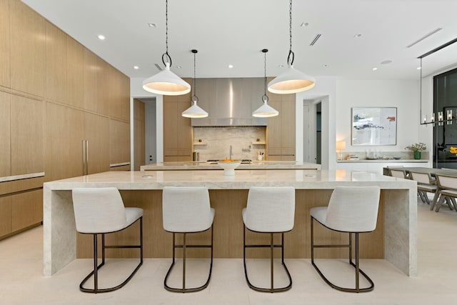 kitchen featuring light stone counters, decorative backsplash, wall chimney range hood, a large island, and modern cabinets