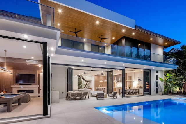 back of house featuring a patio area, a balcony, an outdoor living space with a fireplace, a ceiling fan, and stucco siding