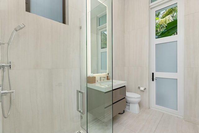 bathroom with toilet, a tile shower, tile walls, and vanity