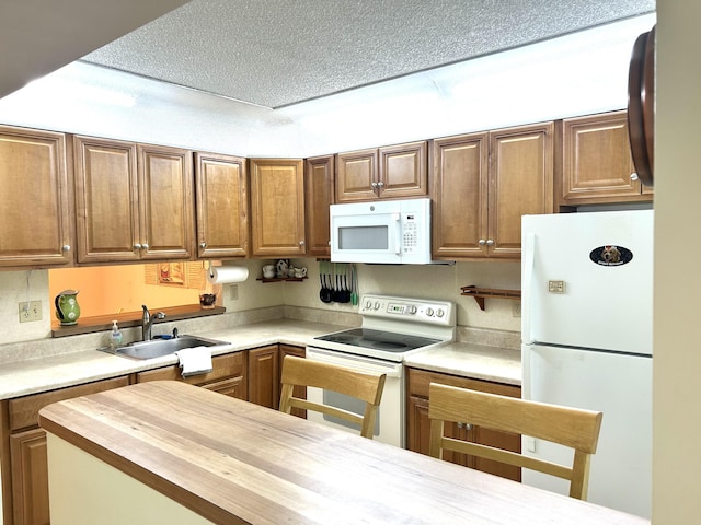 kitchen with white appliances, brown cabinetry, butcher block counters, a textured ceiling, and a sink