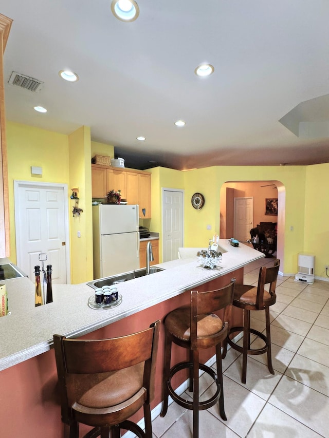 kitchen featuring freestanding refrigerator, visible vents, a breakfast bar area, arched walkways, and a sink