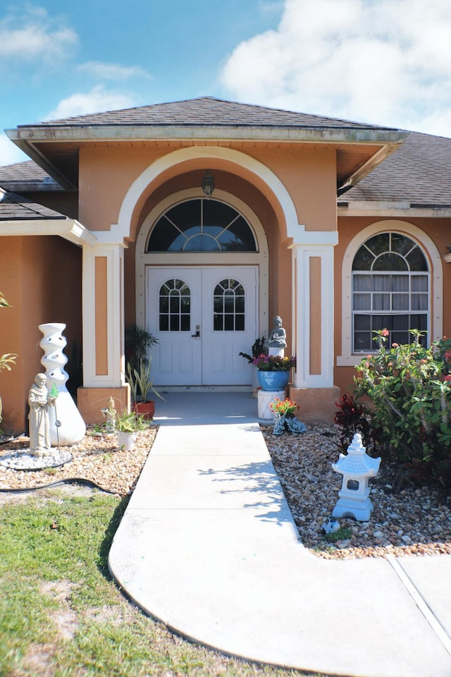 view of exterior entry with roof with shingles, stucco siding, and french doors