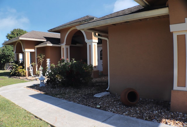 entrance to property featuring a shingled roof and stucco siding
