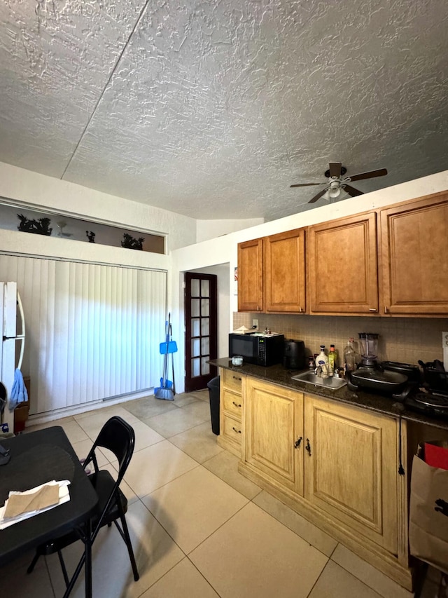 kitchen with a sink, ceiling fan, dark countertops, brown cabinets, and black microwave