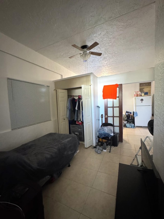 bedroom featuring a closet, light tile patterned floors, a textured ceiling, freestanding refrigerator, and ceiling fan