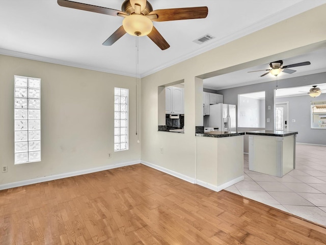 kitchen featuring dark countertops, visible vents, a ceiling fan, white fridge with ice dispenser, and light wood-style flooring