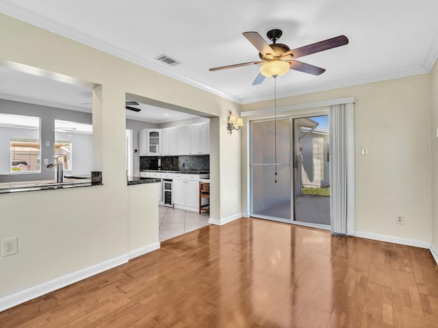 unfurnished living room featuring a ceiling fan, light wood-style floors, baseboards, wine cooler, and visible vents