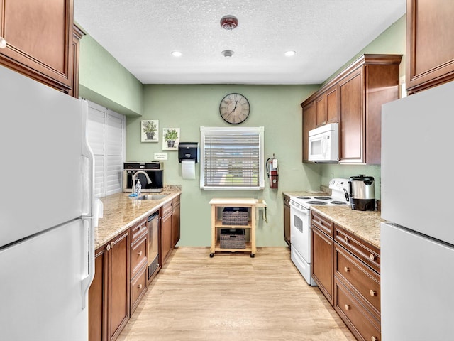 kitchen with a sink, a textured ceiling, white appliances, and light wood-style flooring