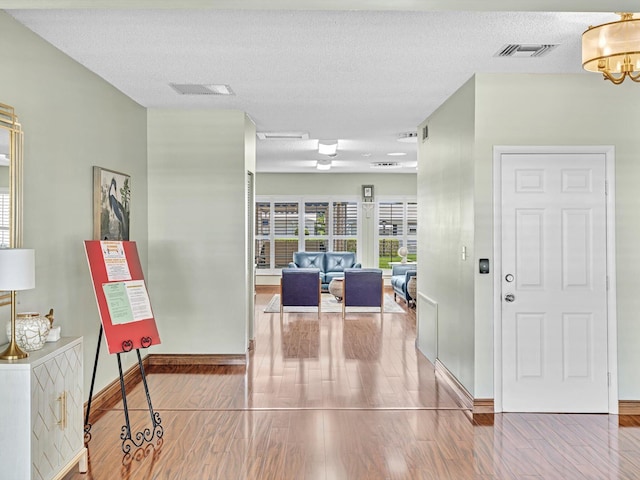 hallway featuring visible vents, wood finished floors, baseboards, and an inviting chandelier