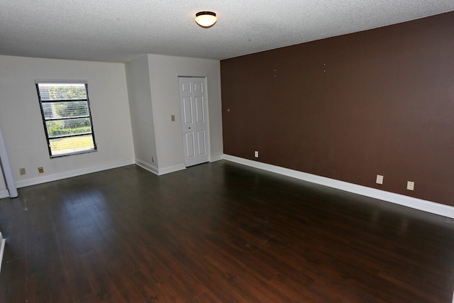 spare room featuring dark wood-style flooring, baseboards, and a textured ceiling