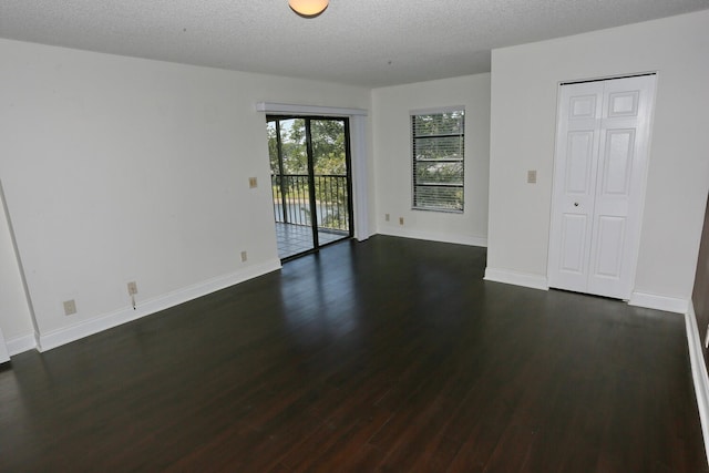 empty room featuring a textured ceiling, baseboards, and dark wood-type flooring