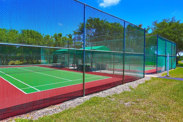 view of tennis court featuring fence and a yard