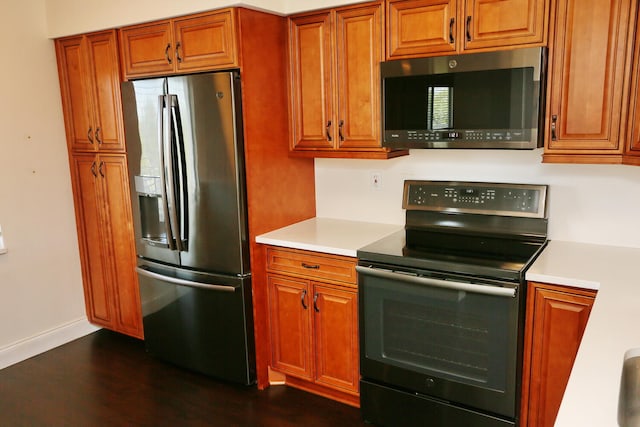 kitchen featuring brown cabinetry, light countertops, dark wood finished floors, and stainless steel appliances