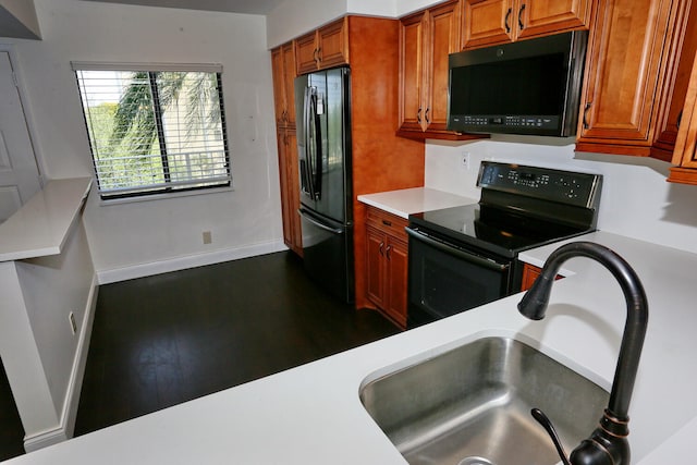 kitchen featuring dark wood-style flooring, a sink, light countertops, baseboards, and black appliances