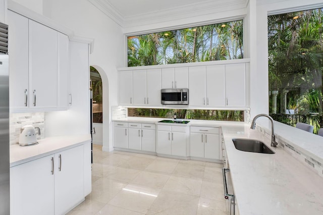 kitchen with tasteful backsplash, a sink, arched walkways, black electric stovetop, and stainless steel microwave
