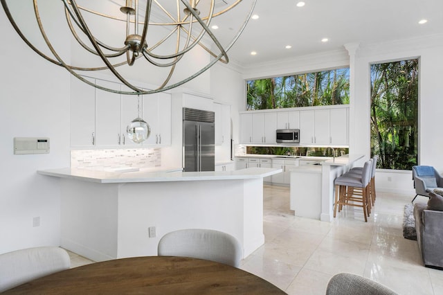kitchen featuring stainless steel appliances, a peninsula, backsplash, light countertops, and a breakfast bar area