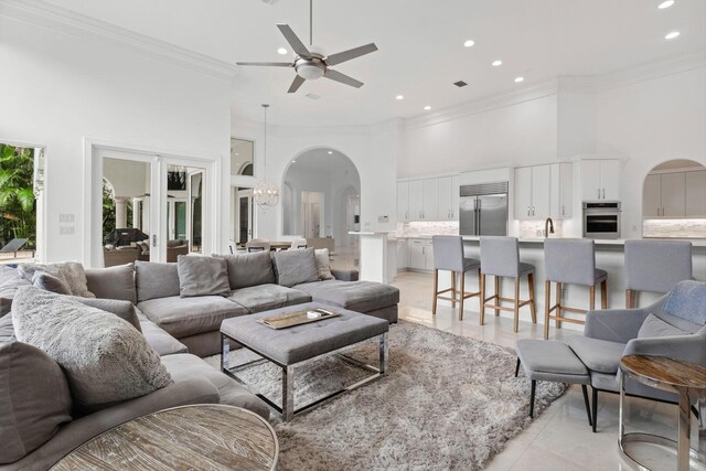 living area featuring crown molding, ceiling fan with notable chandelier, arched walkways, a high ceiling, and recessed lighting