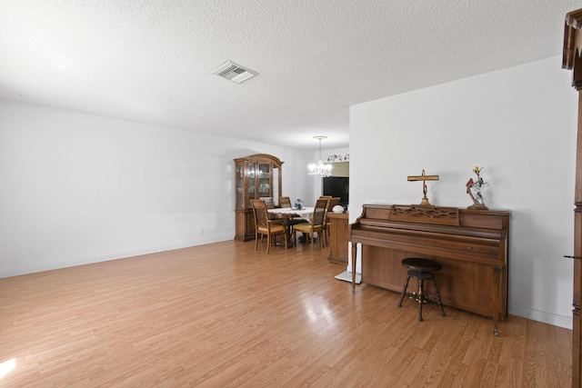 sitting room featuring light wood finished floors, a textured ceiling, visible vents, and a notable chandelier