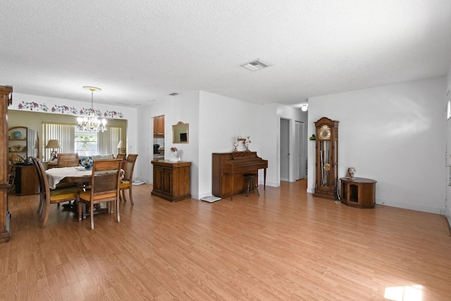 dining space featuring a textured ceiling, a notable chandelier, light wood-type flooring, and visible vents