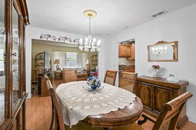 dining room with a notable chandelier, visible vents, light wood-type flooring, and a textured ceiling