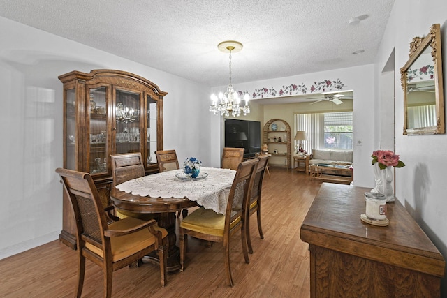 dining space with light wood-style flooring, a textured ceiling, and ceiling fan with notable chandelier