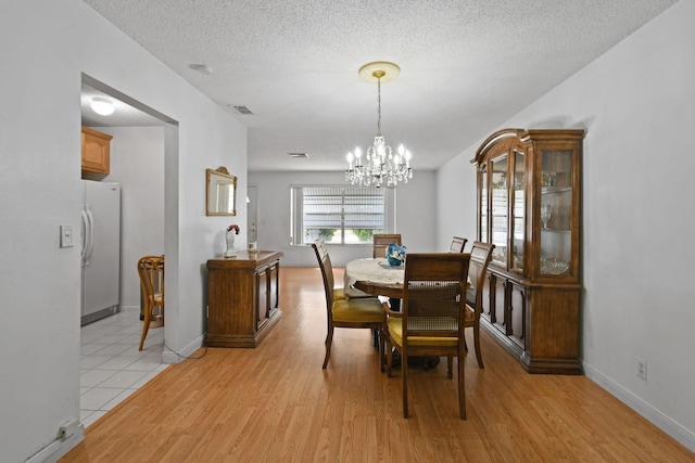 dining area featuring a textured ceiling, light wood-style flooring, baseboards, and a notable chandelier