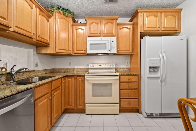 kitchen with stone countertops, white appliances, light tile patterned flooring, and a sink