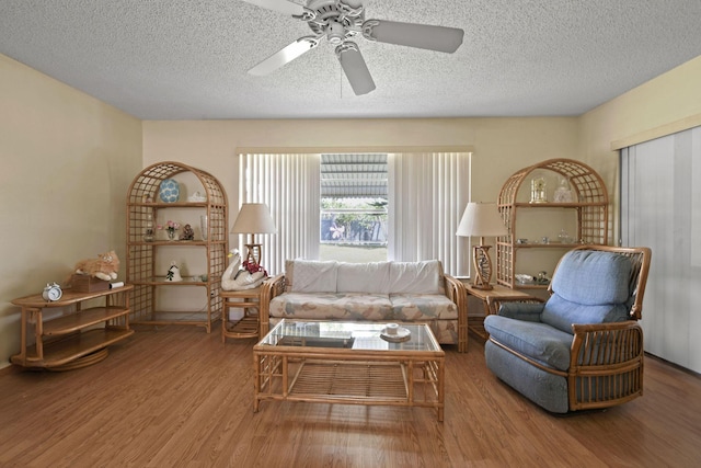 living area with ceiling fan, a textured ceiling, and wood finished floors