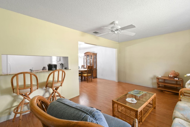 living room with a textured ceiling, a ceiling fan, visible vents, and wood finished floors