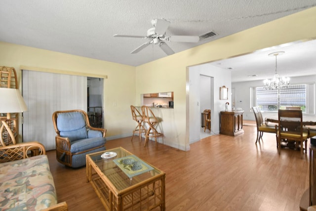 living room featuring a textured ceiling, visible vents, wood finished floors, and ceiling fan with notable chandelier