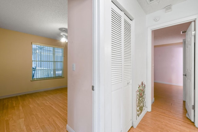 hall featuring baseboards, light wood-style floors, visible vents, and a textured ceiling
