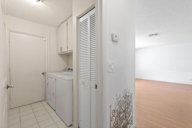 laundry room with washing machine and dryer, a textured ceiling, cabinet space, and visible vents