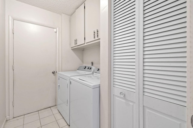 washroom featuring a textured ceiling, light tile patterned floors, cabinet space, and washer and clothes dryer