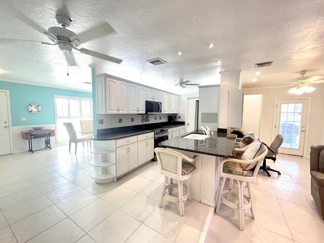 kitchen featuring a ceiling fan, visible vents, a kitchen bar, appliances with stainless steel finishes, and a sink