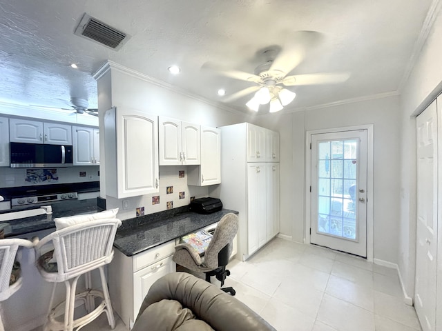 kitchen with dark stone countertops, visible vents, ornamental molding, ceiling fan, and stainless steel microwave
