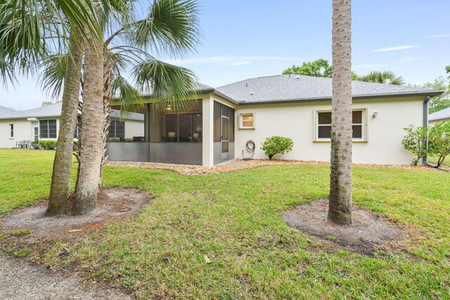 back of house featuring a sunroom, roof with shingles, stucco siding, and a lawn