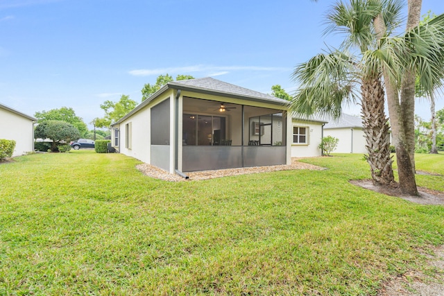 back of property with stucco siding, a sunroom, and a lawn