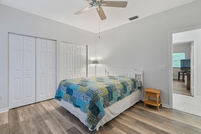 bedroom featuring two closets, ceiling fan, visible vents, wood finished floors, and baseboards